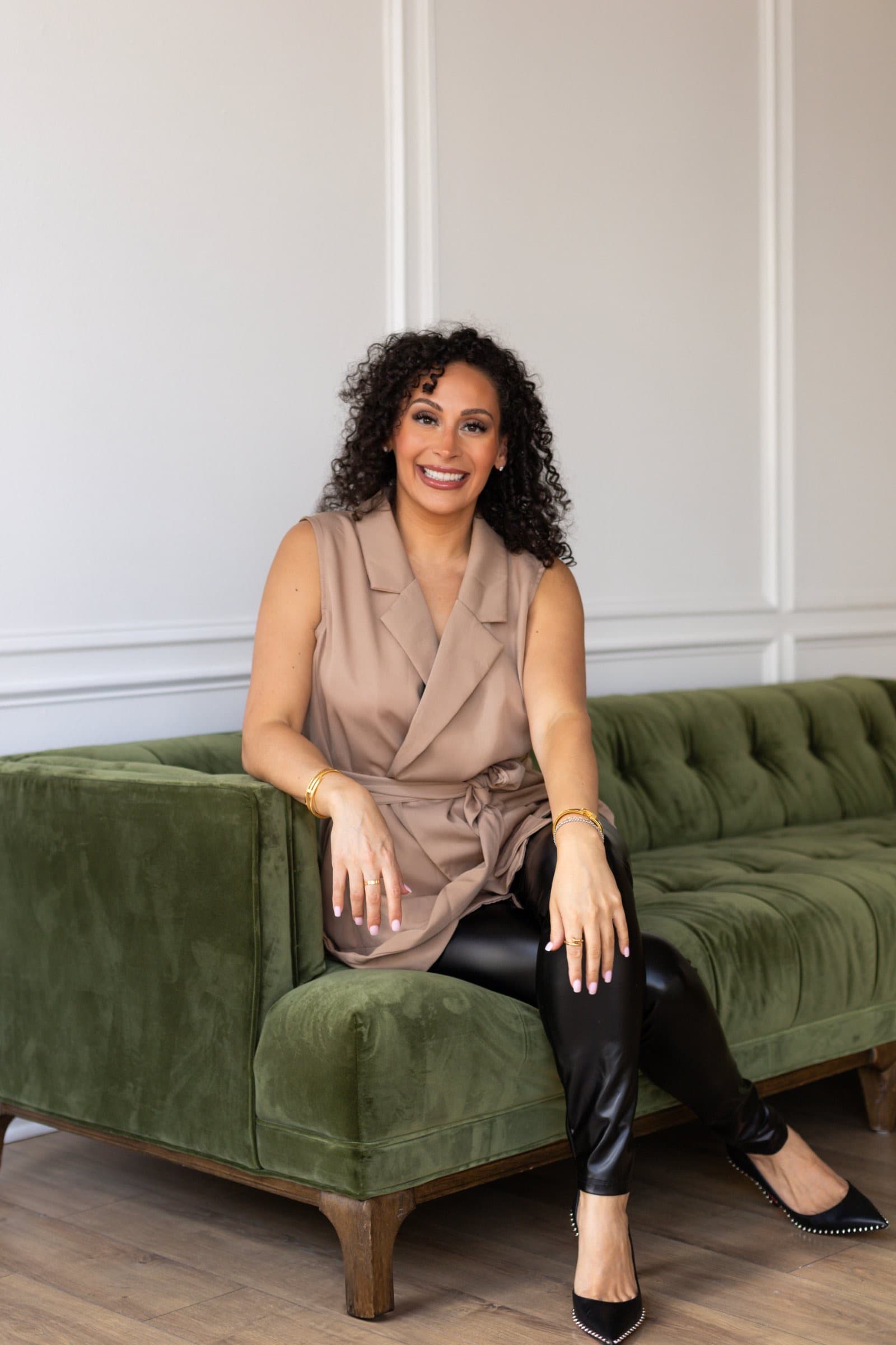 Dr. Shaggy of Veneer Lounge seated on a green velvet sofa, smiling.